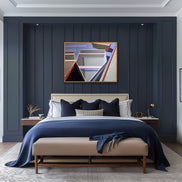 Artist Shilo Ratner, Abstract boat art painting, By the Dock, with geometric shapes in a modern bedroom with dark blue paneled walls, a bed with blue bedding, and abstract art above the bed.