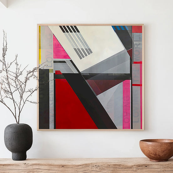 A framed original  abstract geometric painting by Shilo Ratner with mantra I am loving Awareness in the underlayer, with bold red, pink, gray, black, and white shapes hangs on a white wall above a wooden console table. 